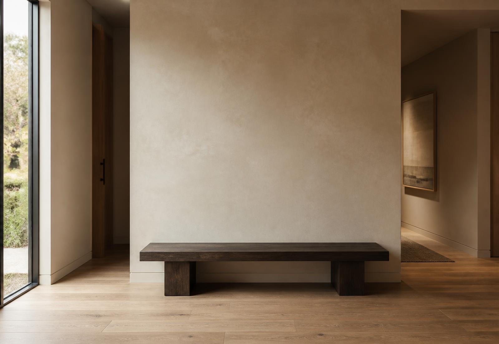 Warmes, minimalistisches Entrée mit beige Wand, dunkler Bank und Eichenboden